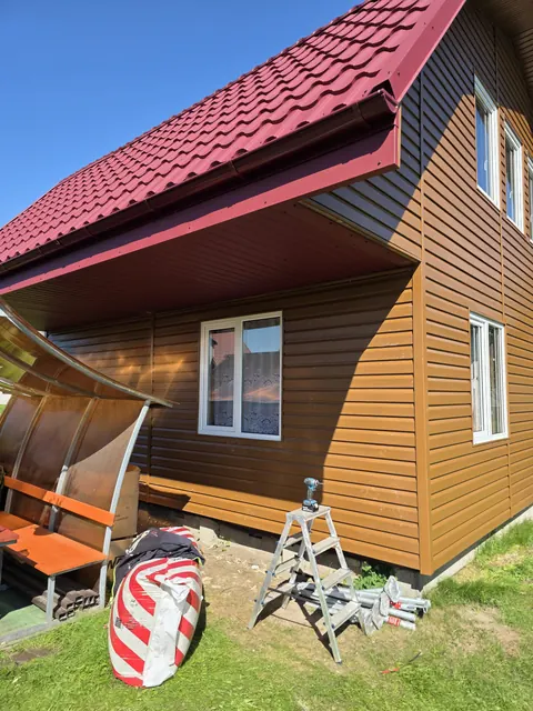 Atnaujintas rudas fasadas po raudonu stogo kraštu